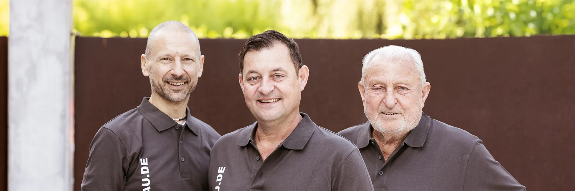 Drei Männer in Poloshirts von Luczky-Bau vor einer rostroten Stahlwand