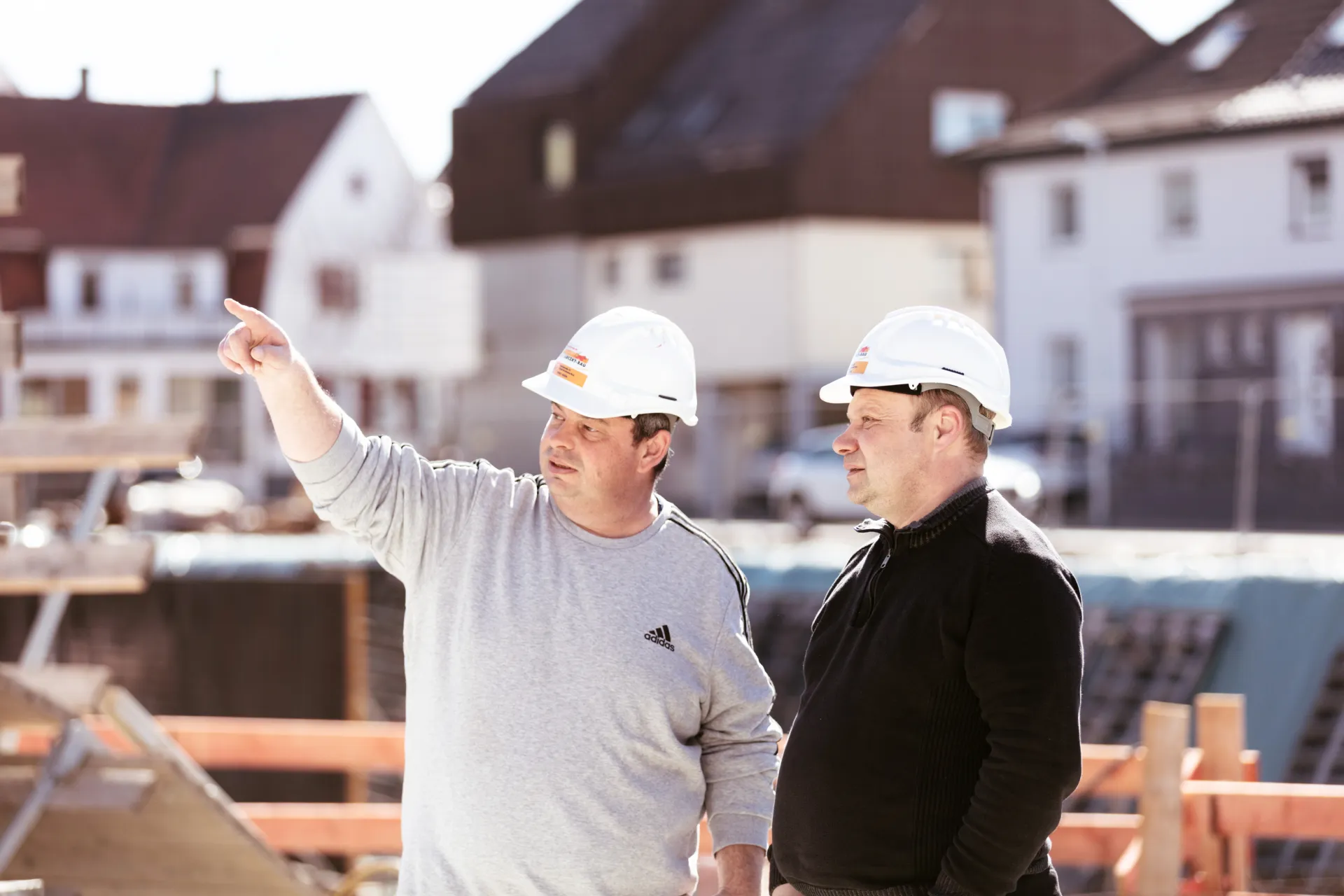 Zwei Bauleiter mit Helmen auf der Baustelle, einer zeigt in die Ferne
