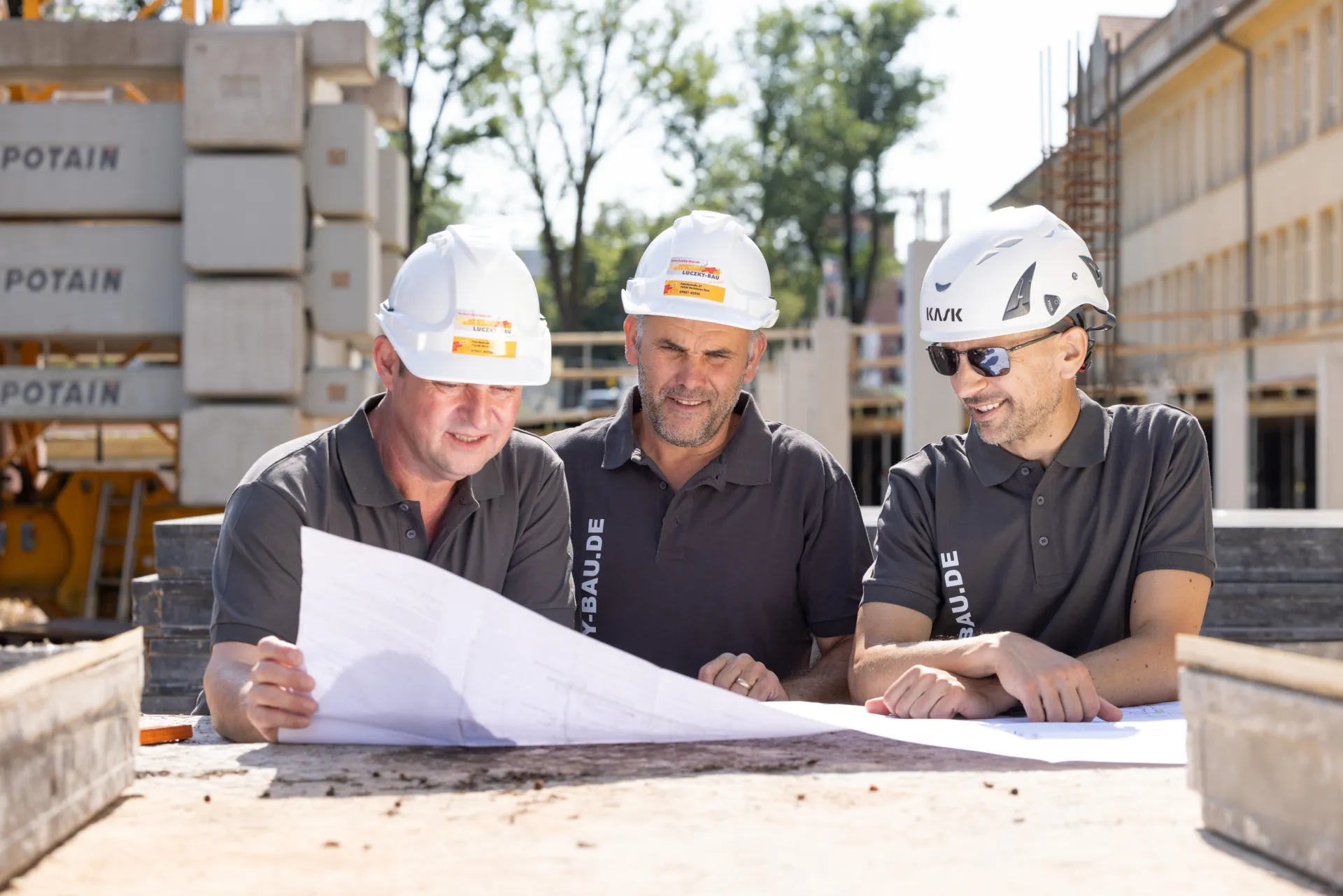 Drei Bauleiter mit Helmen besprechen einen Plan auf der Baustelle