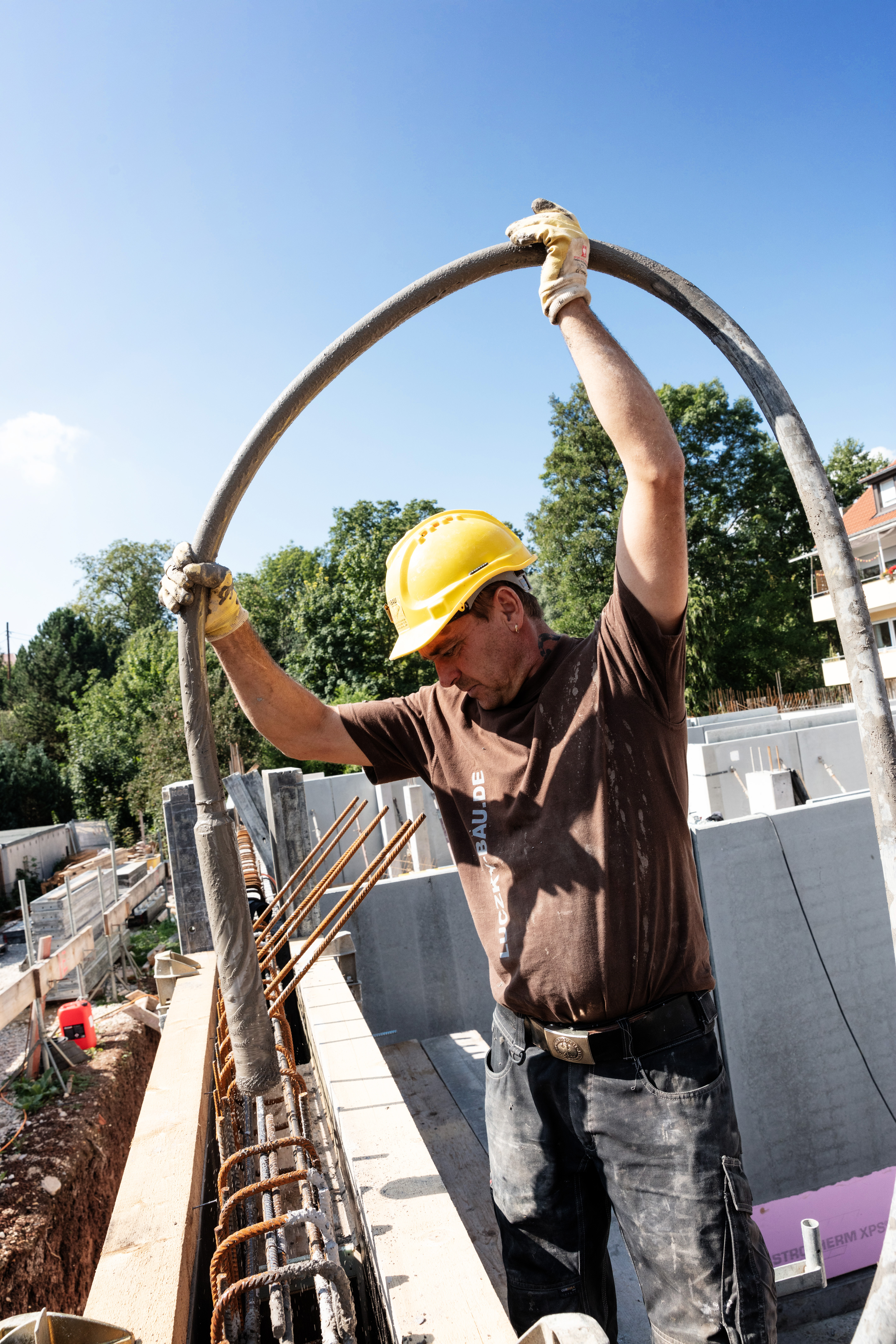 Mitarbeiter mit gelbem Helm biegt Bewehrungsstahl