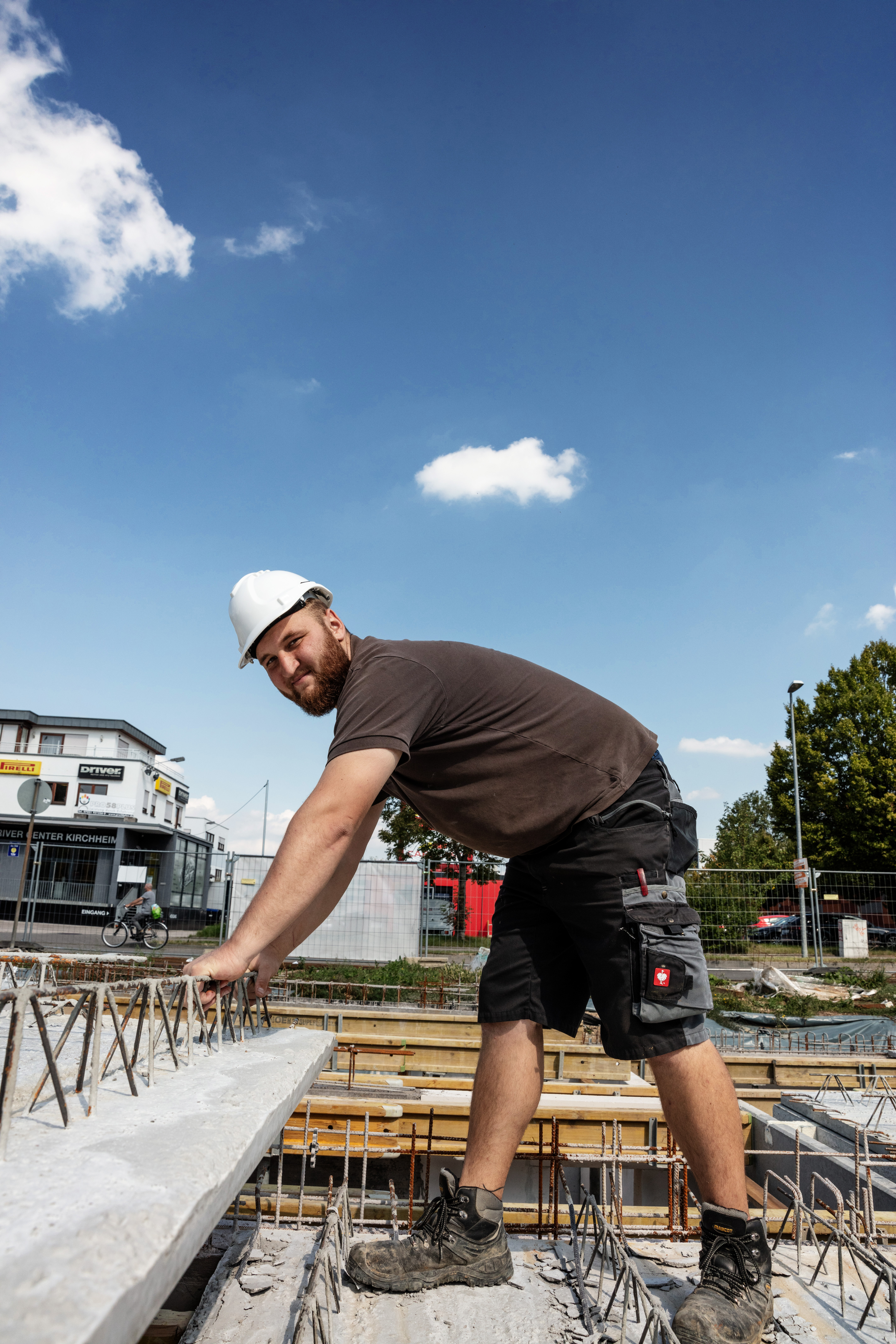 Mitarbeiter mit Helm arbeitet an einer Bewehrung vor einem Neubau