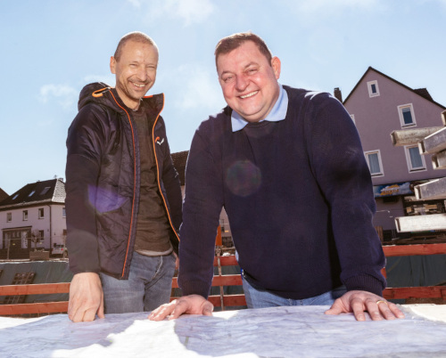 Zwei Männer von Luczky-Bau beugen sich lachend über einen Bauplan